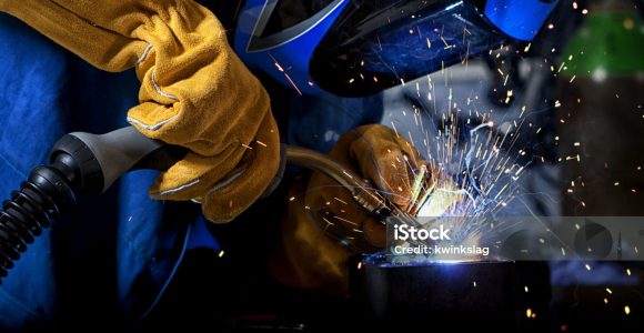 Welder wearing gloves and mask with welding sparks.